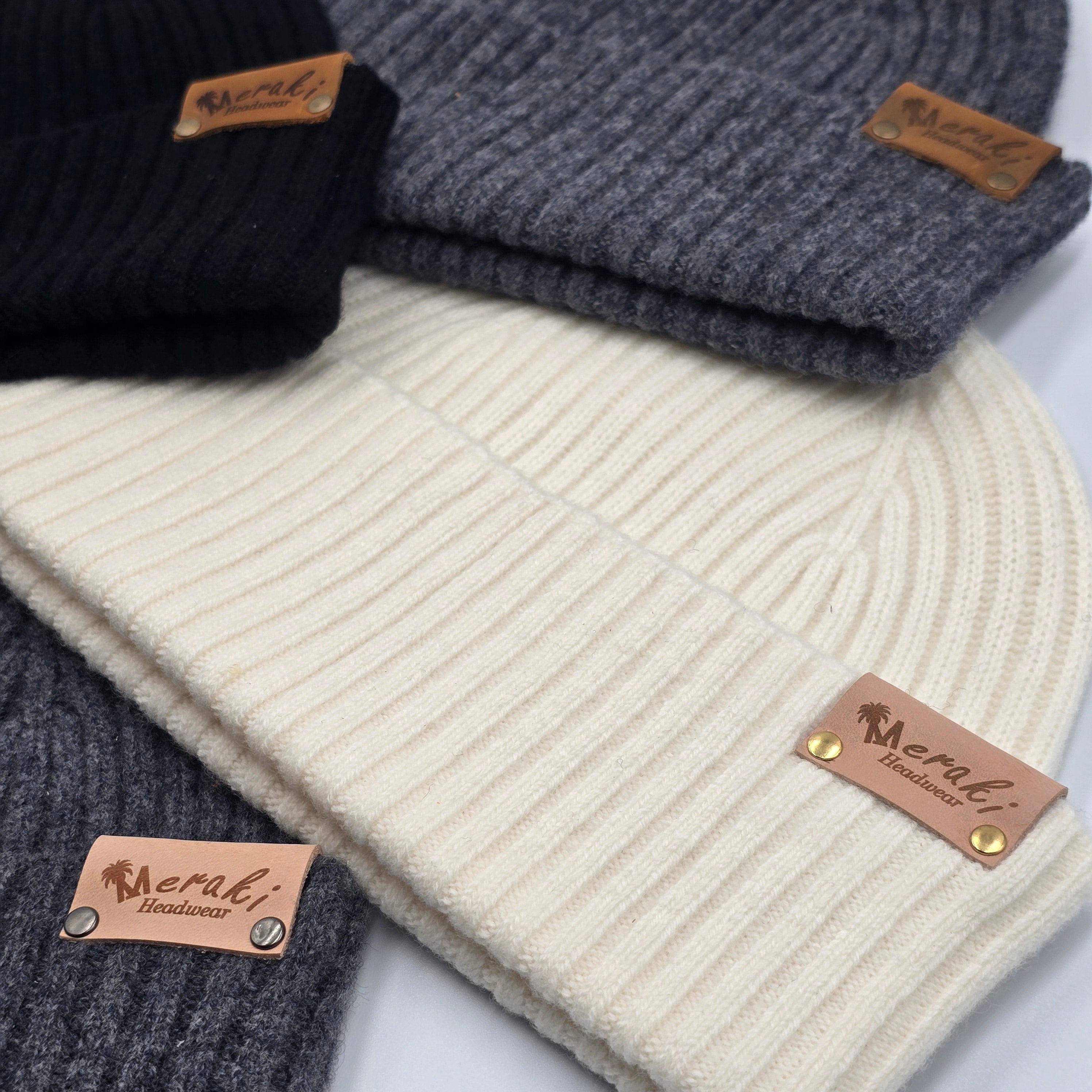 Three knit hats in gray, black, and white with 'Meraki' brand tags on a light background. variant-Charcoal variant-Black variant-Cream